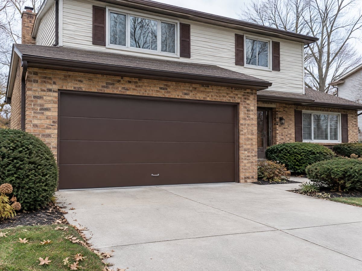 Garage door repair for a two-story brick and siding house with a dark brown two-car garage door and a clean driveway.