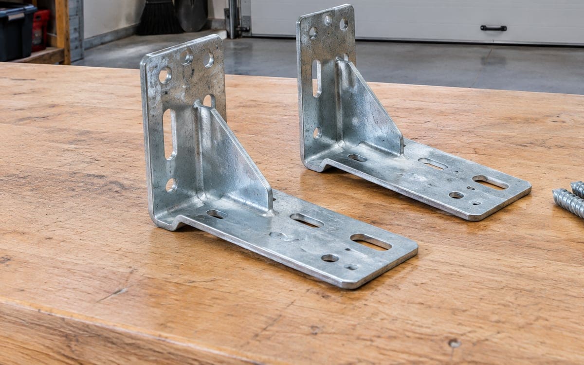 Two new galvanized jamb brackets on a workbench, the parts a garage door track repair bolts to the jamb.
