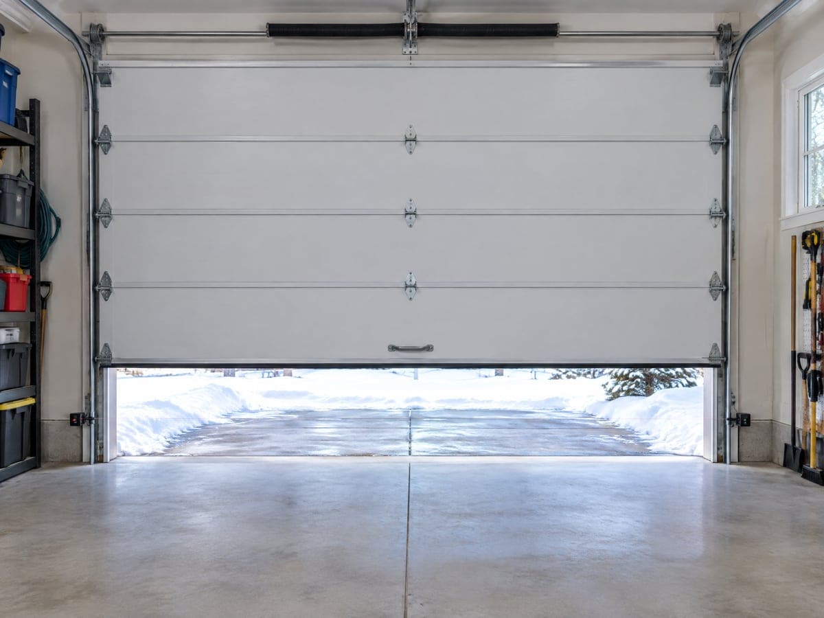 When a garage door won't open all the way: a white door stopped about a foot above the floor, snow on the driveway beyond.