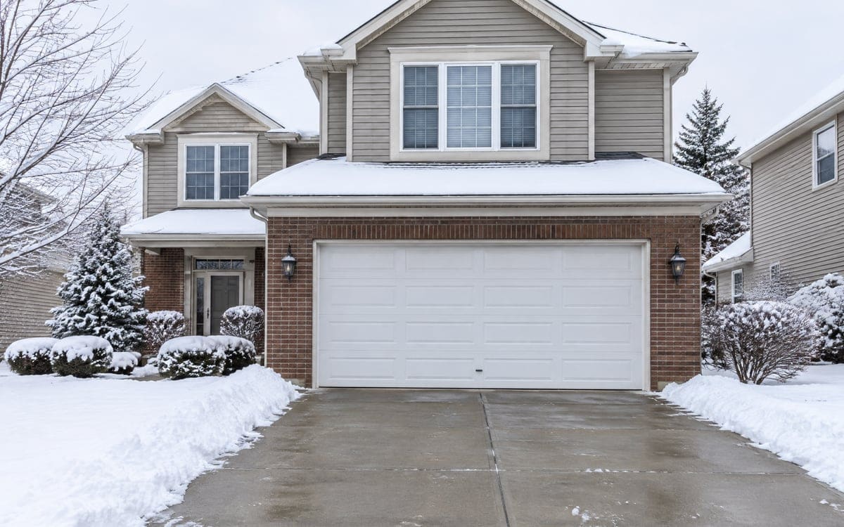 Garage door insulation on an attached garage: a white two-car door on a two-story house after a snowfall.