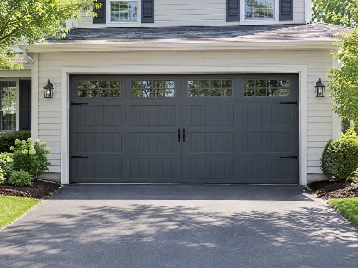 A finished garage door installation: a dark gray carriage-style two-car door with window panels on a white house.