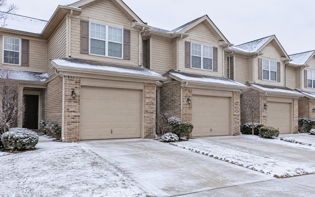 Garage door repair for townhomes: a row of matching tan doors after a light snow.